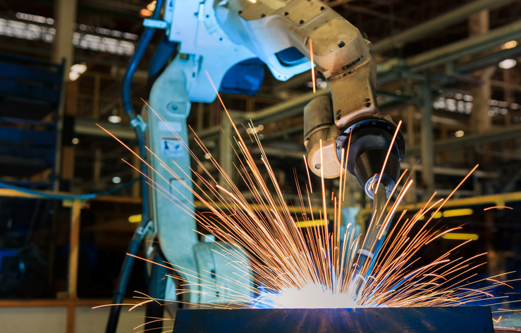 A blue robot welds metal in a factory. The advantages of robotic welding include efficiency and safety.
