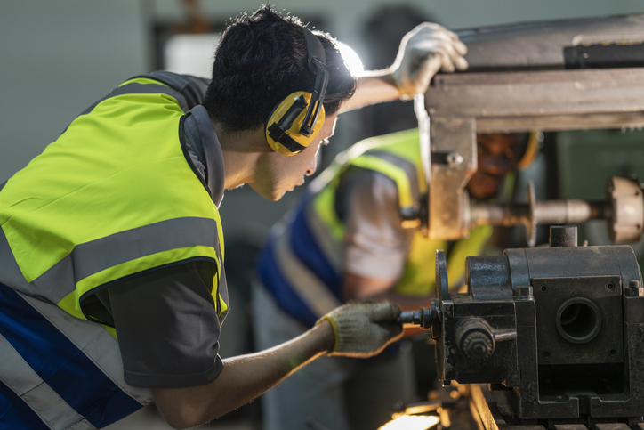 A skilled technician works attentively on a heavy duty machine in an industrial workshop for a custom manufacturing company.